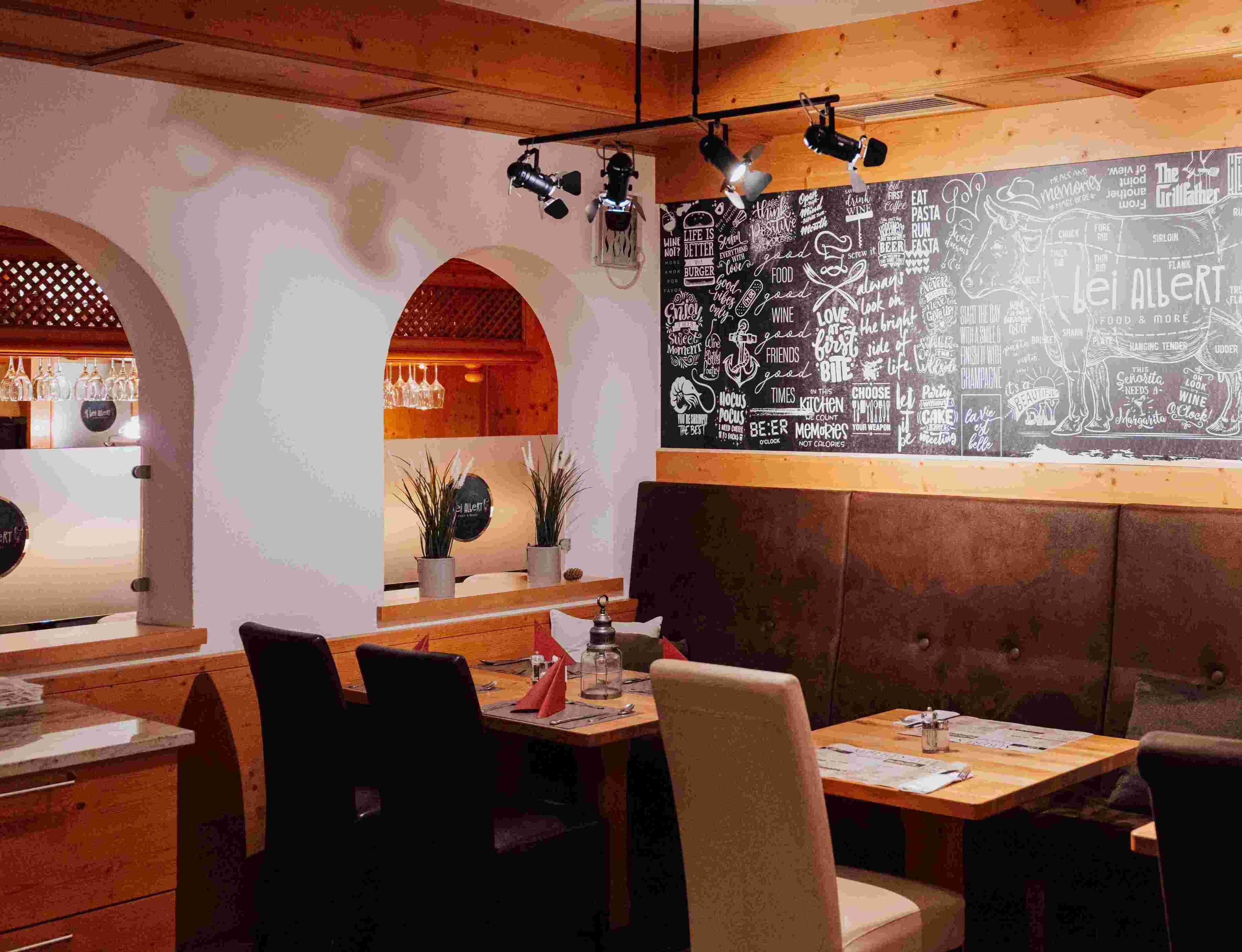 A restaurant interior with wooden booths, a chalkboard wall with various phrases, and hanging lights.