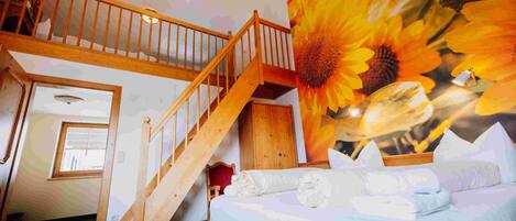 Una habitación con una cama, una escalera de madera y un cuadro grande de un girasol.