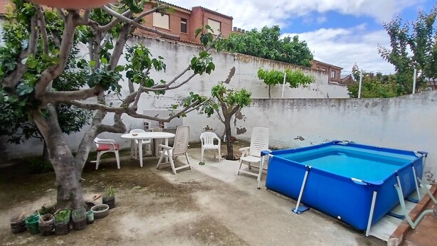 A backyard with a blue pool, white plastic chairs, a small table, and potted plants. - Room-double Room With Air Conditioning i (Toledo)