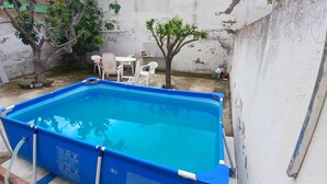 A rectangular pool with a blue border, surrounded by a concrete wall. There are white plastic chairs and a small tree in the background. - Room-double Room With Air Conditioning i (Toledo)