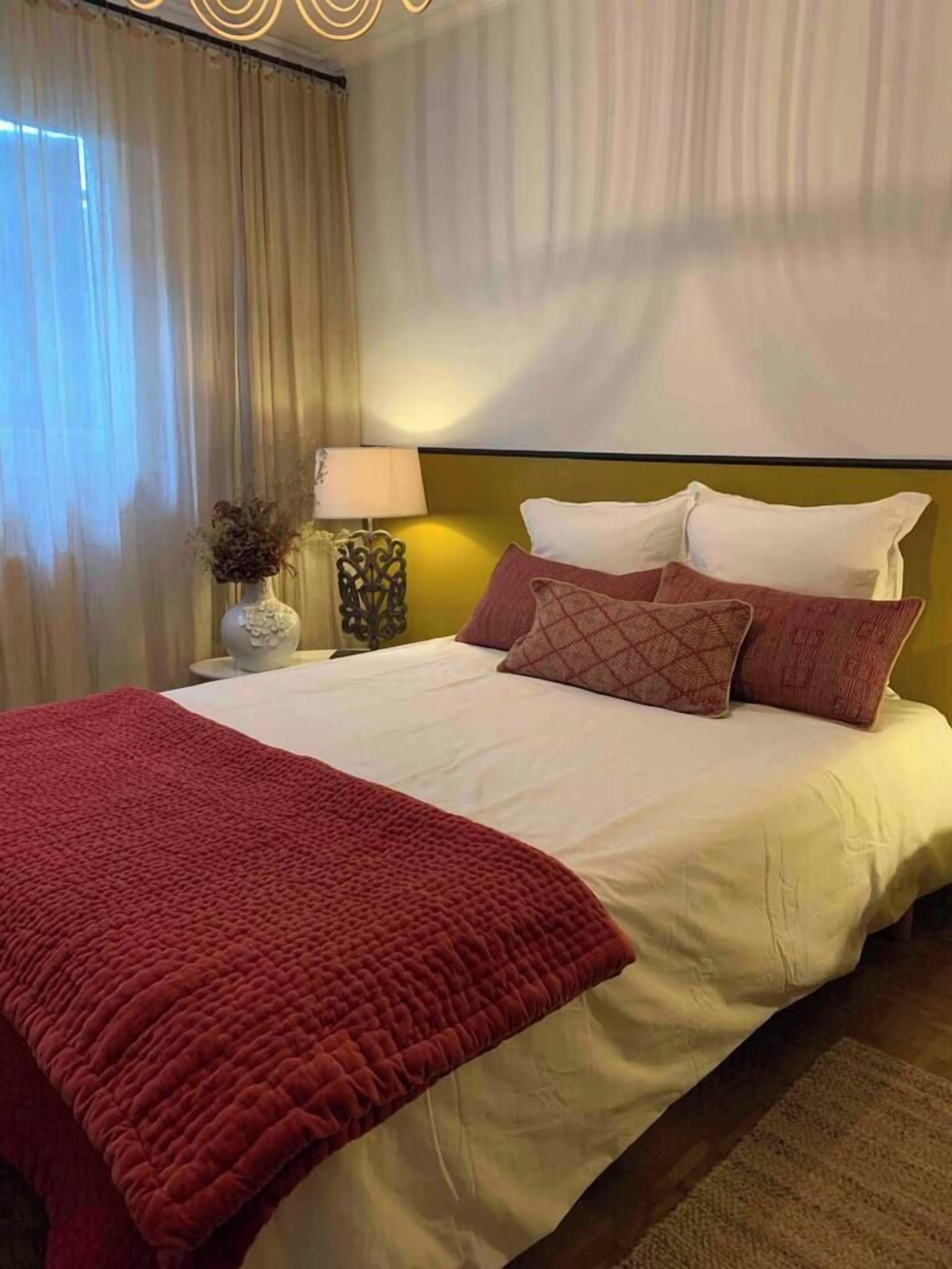Une chambre d’hôtel avec un lit, une table de chevet, une lampe et un vase contenant des fleurs séchées.