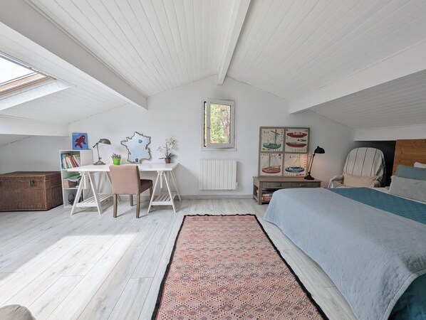 A bedroom with a bed, a desk, a chair, a radiator, a window, and a bookshelf.