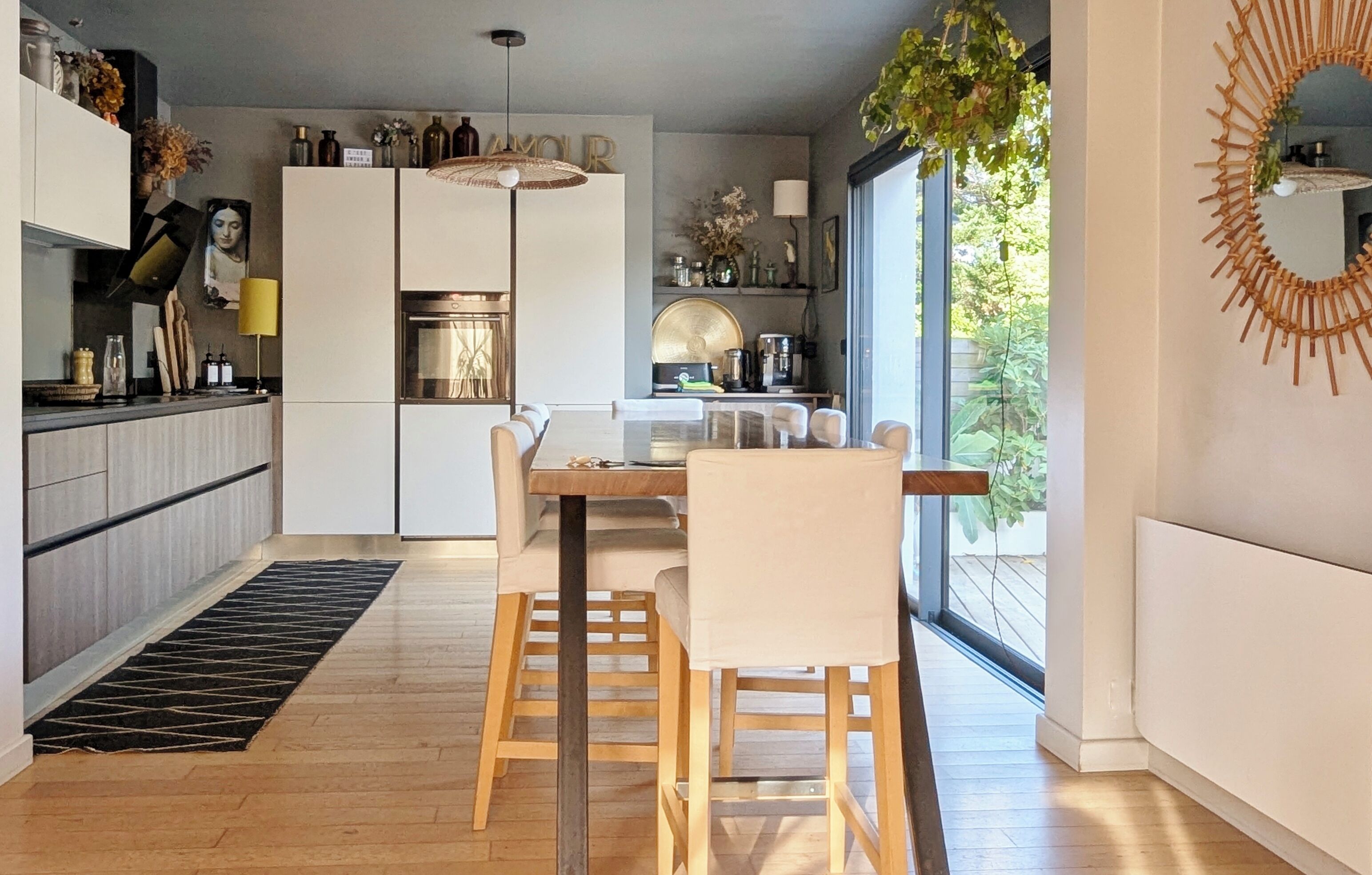 Una cocina moderna con zona de comedor, suelo de madera y un amplio ventanal que proporciona luz natural.