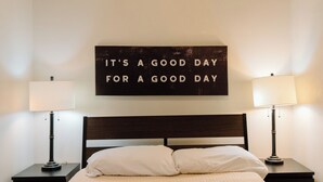 A neatly made bed with a white comforter and two pillows, flanked by two bedside tables with lamps, and a motivational sign on the wall. - Modern 2 Bedroom Downtown Apartment (Milwaukee)