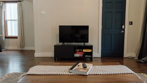 A living room with a flat-screen TV on a black stand, a wooden coffee table with a magazine and remote, and a door with a key in the lock. - Modern 2 Bedroom Downtown Apartment (Milwaukee)