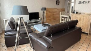 A living room with a sofa, a coffee table, a TV, and a lamp. - Gîte L'Elixir (Fécamp)