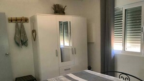 Une chambre à coucher comprenant un lit, une armoire, une petite table et une fenêtre avec des stores.