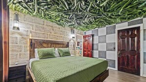 Ein Schlafzimmer mit Bett, Holz-Kopfteil, grüner Bettwäsche, einer Ziegelwand, Holzboden und einer Decke mit hängenden Pflanzen.