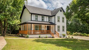 Een huis met twee verdiepingen, een overdekte veranda en voortuin.