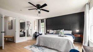 Een slaapkamer met een bed, een plafondventilator, een nachtkastje, een stoel, een spiegel en een raam.