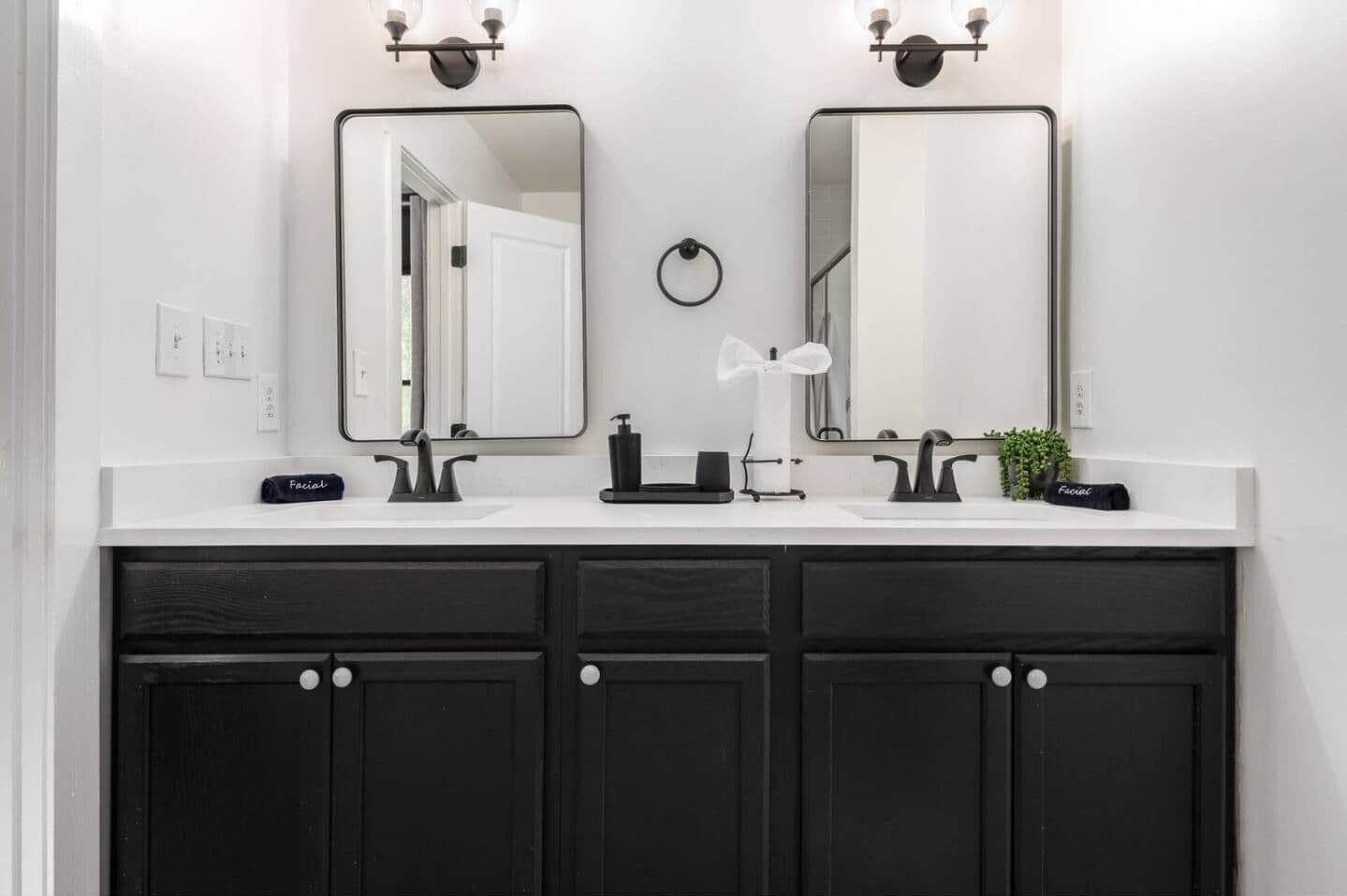 A bathroom with two mirrors, a white countertop, black cabinets, and a small plant.