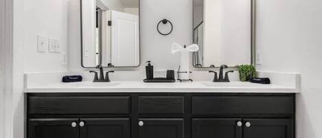 A bathroom with two mirrors, a white countertop, black cabinets, and a small plant.