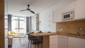 A modern kitchen with a wooden countertop, white cabinets, and a built-in microwave. There is a dining area with a yellow chair and a sofa.