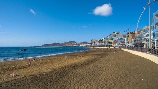 A beach with a clear sky, a sandy shore, and buildings along the coastline.