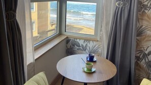 A room with a view of the sea, a round table with a cup, and two yellow armchairs.