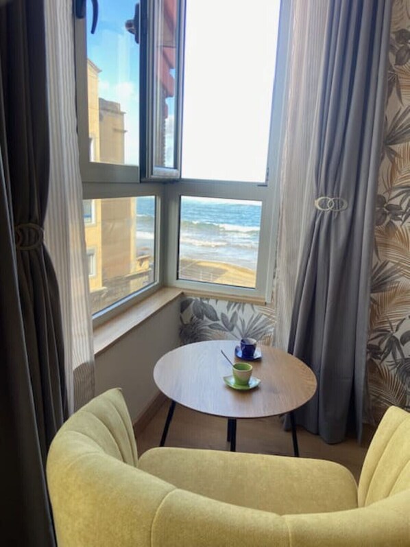 A room with a view of the sea, a round table with a cup, and two yellow armchairs.