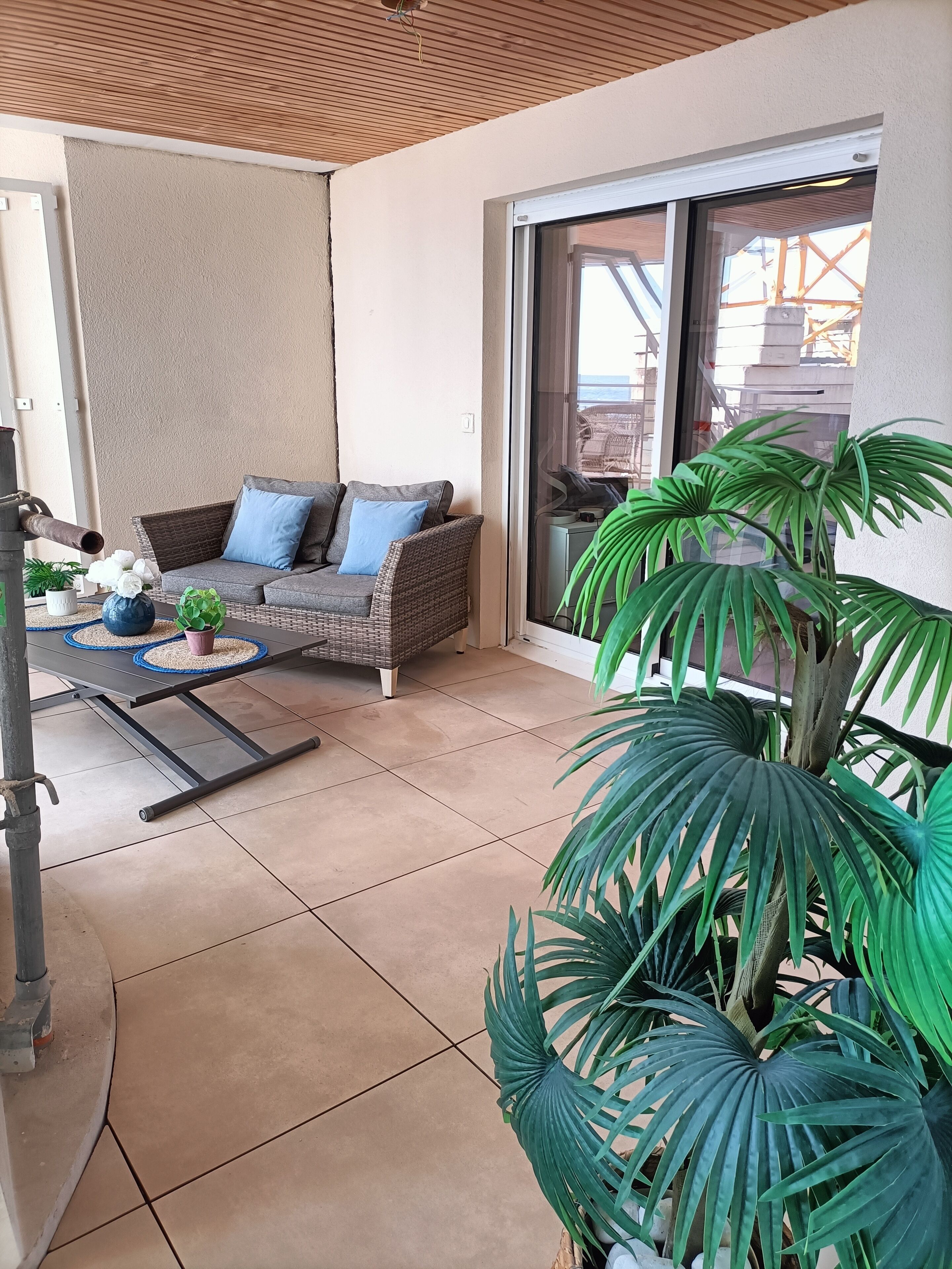 Een balkon met een rieten bank, een eettafel en potplanten.