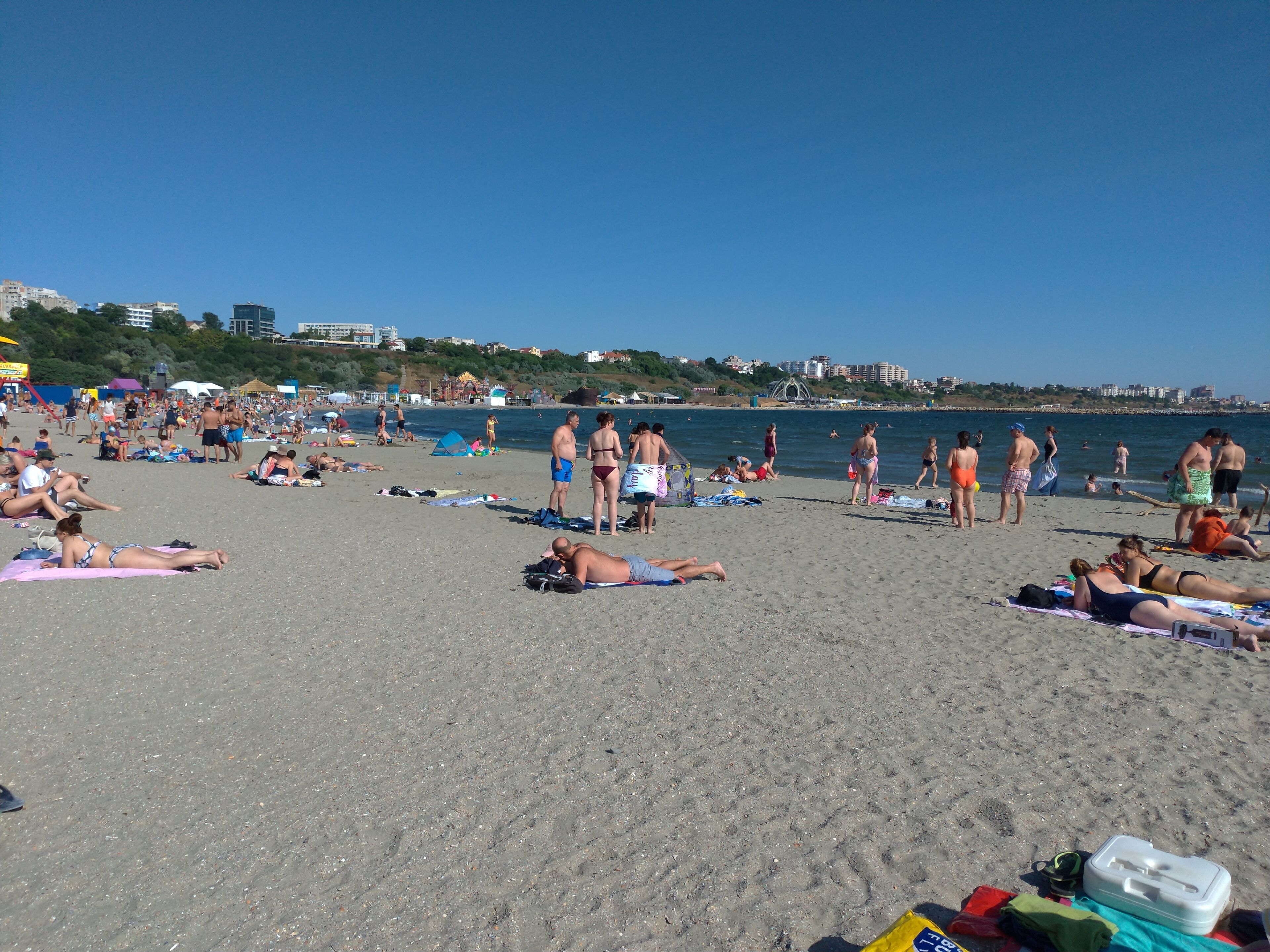 Una playa concurrida, gente tomando el sol y nadando.