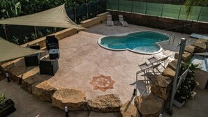 A backyard with a swimming pool, lounge chairs, a barbecue grill, and a decorative star pattern on the ground.