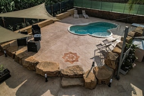 Um quintal com piscina, cadeiras de descanso, churrasqueira e um padrão decorativo em formato de estrela no chão.