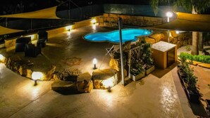 A nighttime outdoor pool area with a blue pool, stone seating, and a canopy.