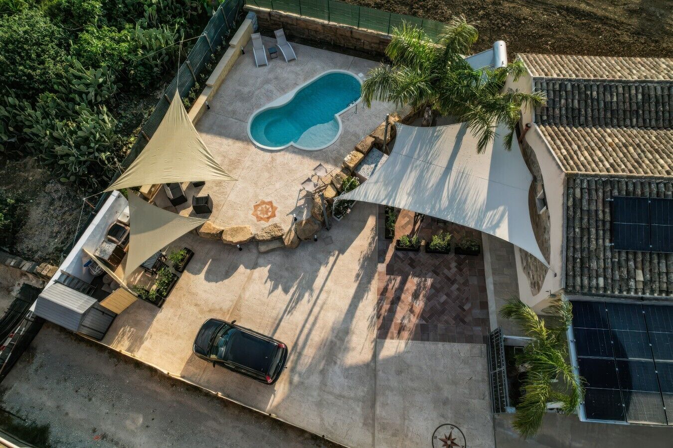 Vista aerea di una proprietà residenziale con piscina, area relax esterna, automobile e pannelli solari.