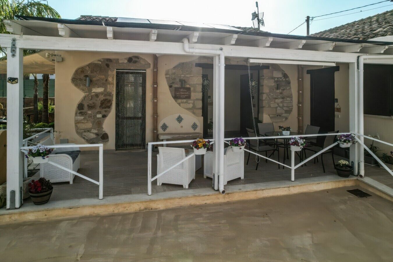 Un espace extérieur abrité, avec des tables et des chaises, des murs en pierre et une porte.