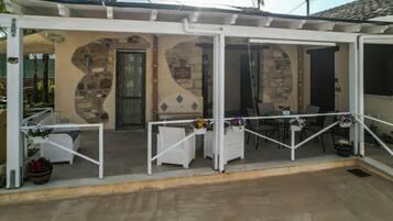 Un espace extérieur abrité, avec des tables et des chaises, des murs en pierre et une porte.