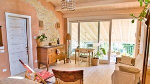 A cozy room with a wooden ceiling, a large sliding glass door leading to an outdoor area, a wooden dresser, a chair, and a bed with a patterned bedspread.