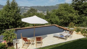 A swimming pool with a wooden deck, lounge chairs, and a large umbrella.