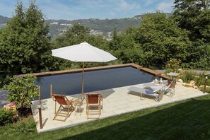 A swimming pool with a wooden deck, lounge chairs, and a large umbrella.