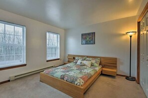 Un dormitorio con cama de madera, dos ventanas, una lámpara de pie y un cuadro en la pared.