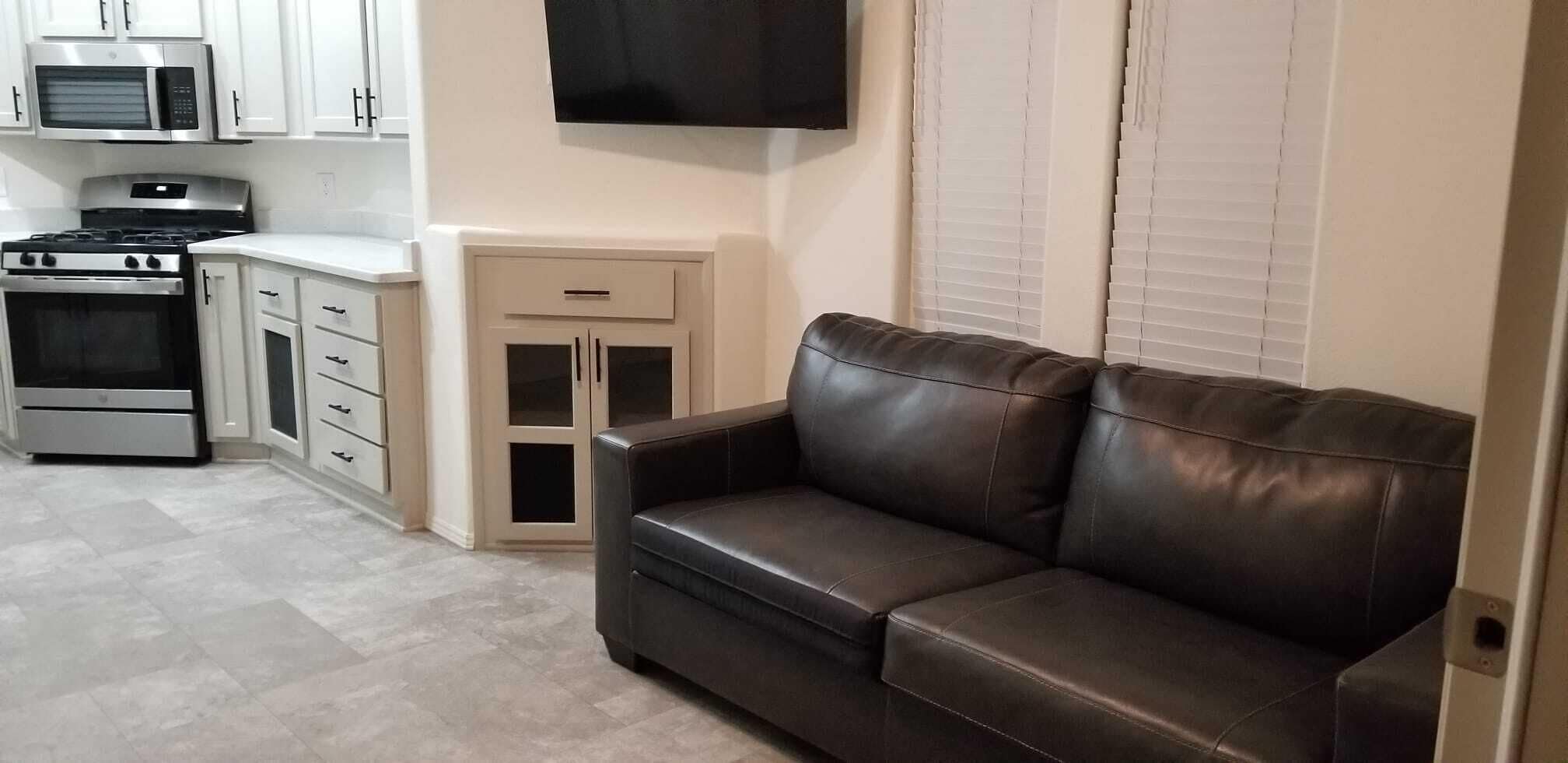 A compact living space with a kitchenette, a sofa, and a TV mounted on the wall.