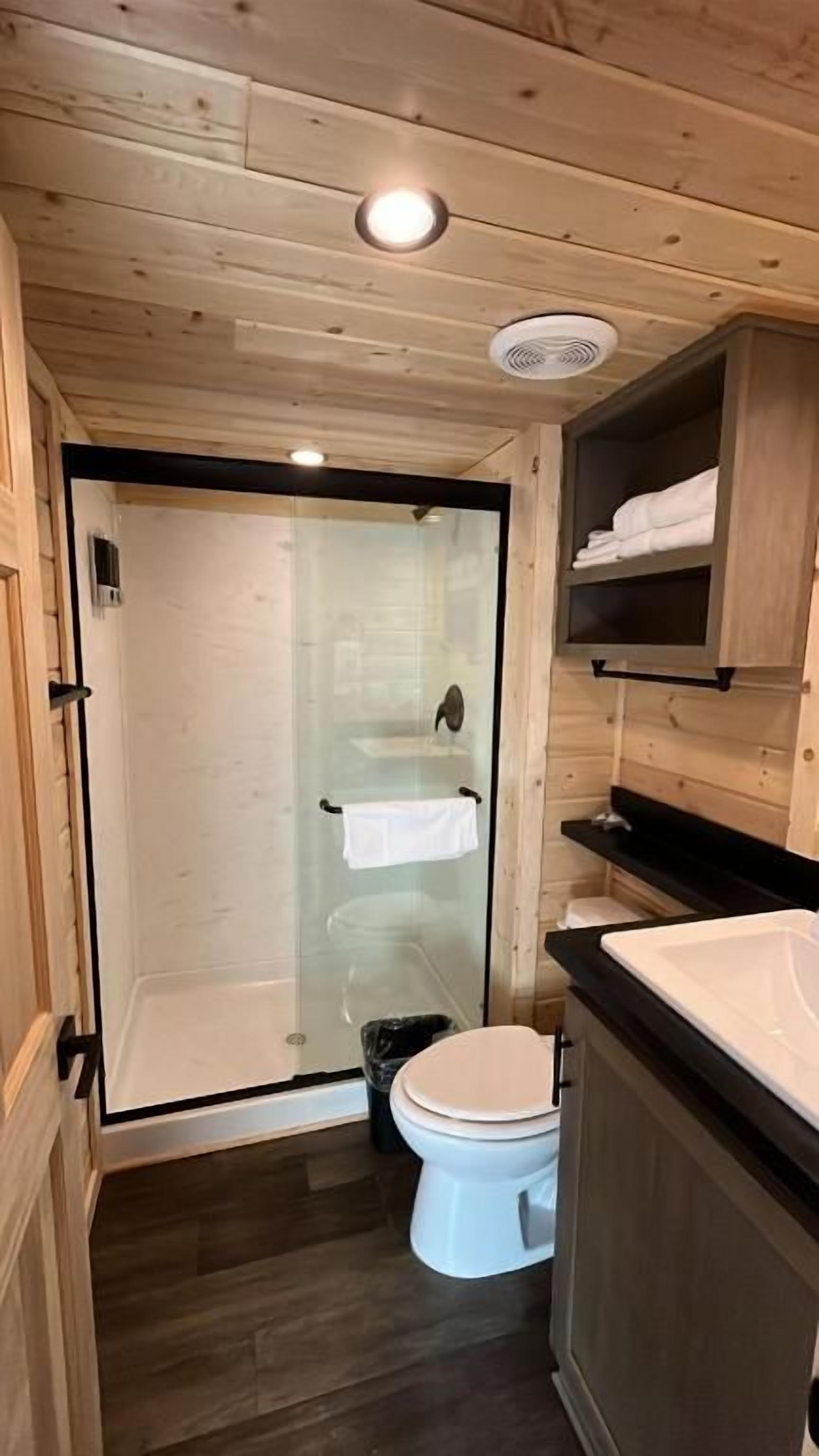 Un baño con cabina de ducha de vidrio, inodoro blanco y muebles de madera.