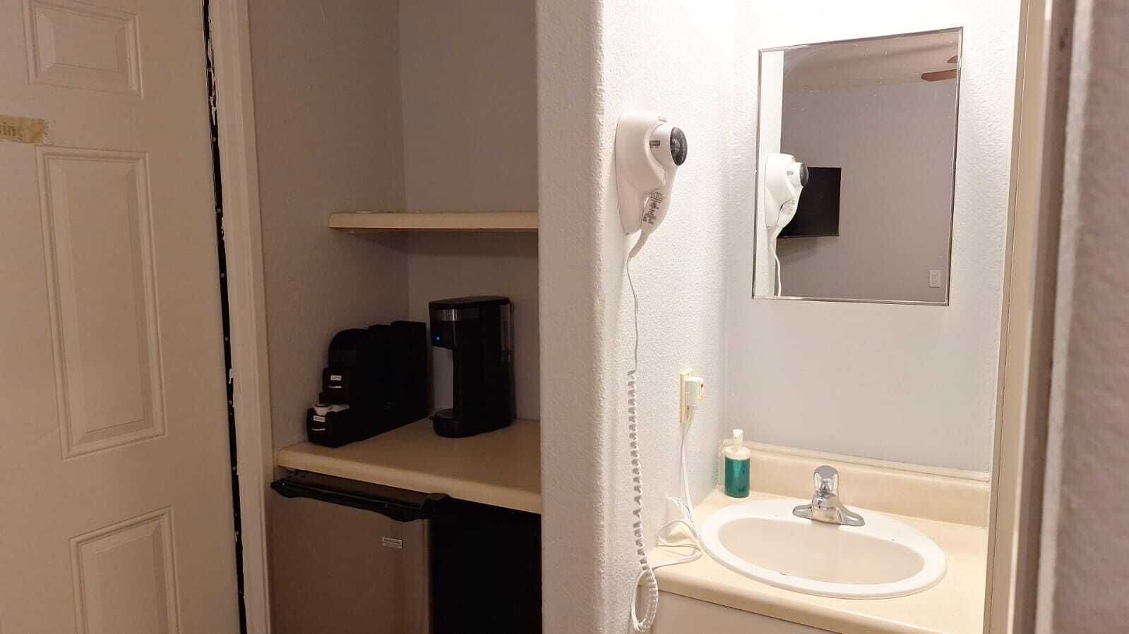 Ein Badezimmer mit Waschbecken, Spiegel, Föhn und Kaffeemaschine.