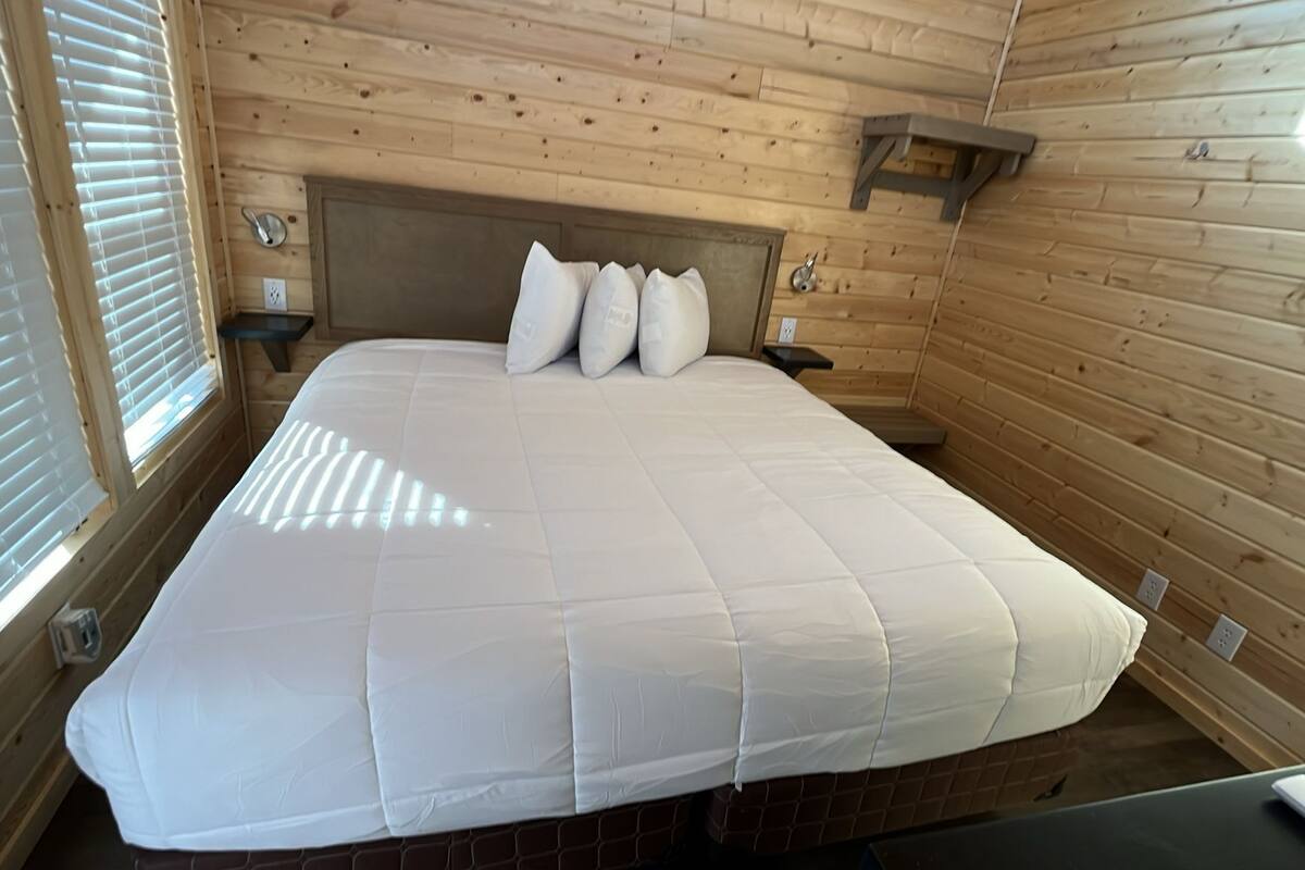 A bedroom with a large bed, wooden walls, a headboard, bedside tables, and a window with blinds.