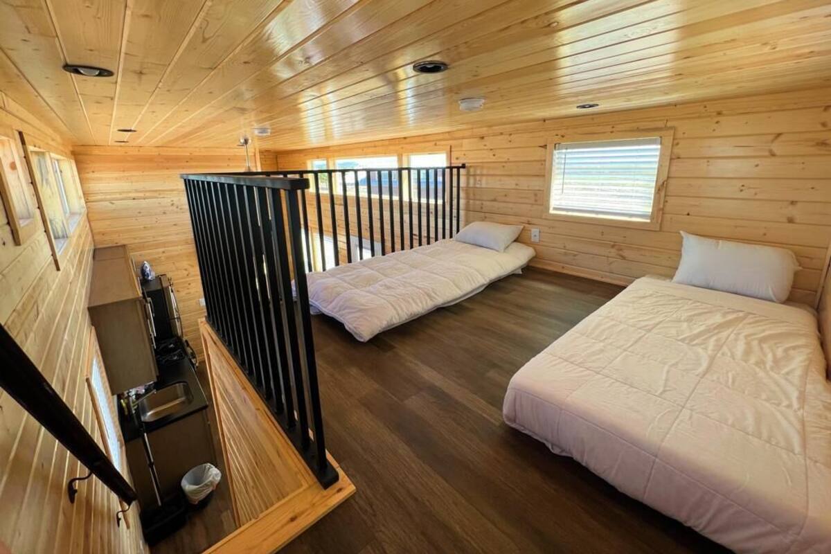 A cabin with two beds, a small kitchenette, and a balcony with a railing.