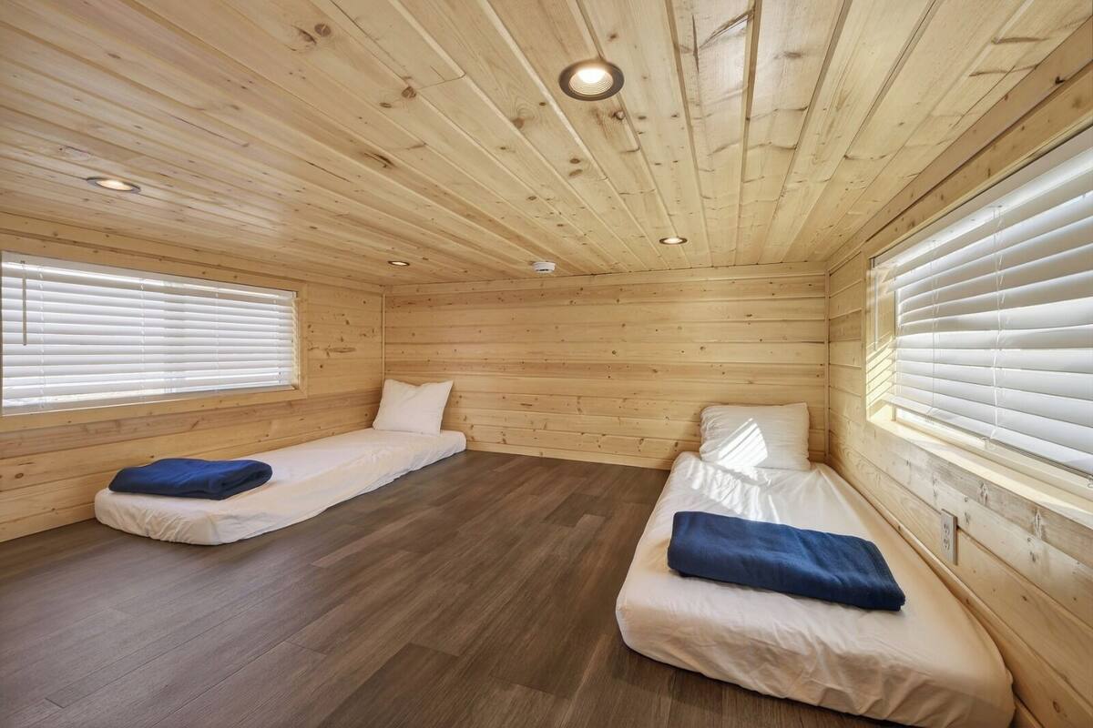 A cabin with two single beds, wooden walls, and a sloped ceiling with recessed lighting.