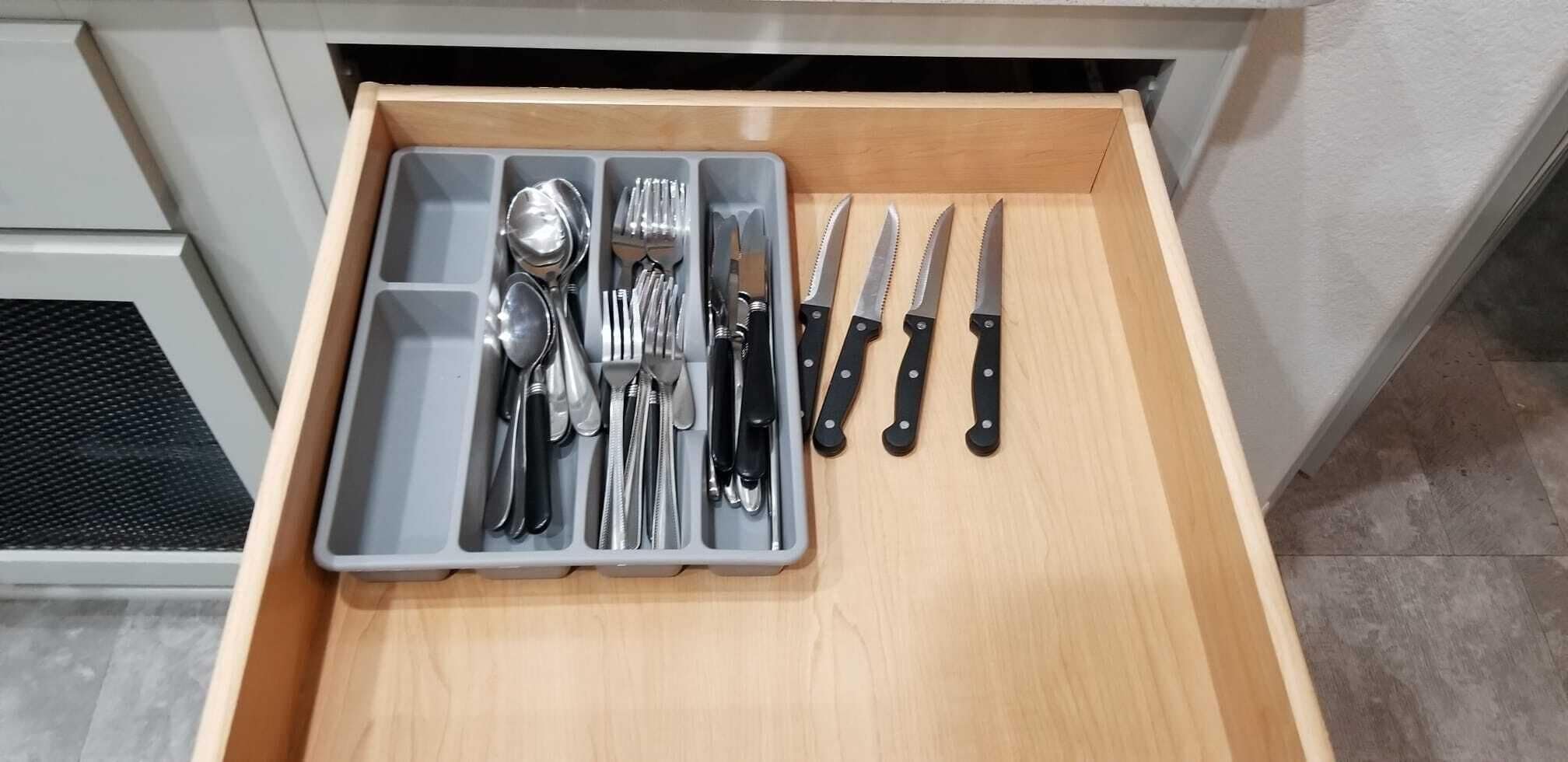 Eine Küchenschublade mit Besteck und Messern, ordentlich in Fächern angeordnet.
