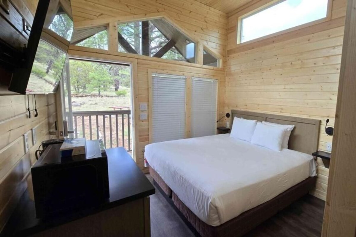 A wooden cabin bedroom with a bed, a desk, and a window.