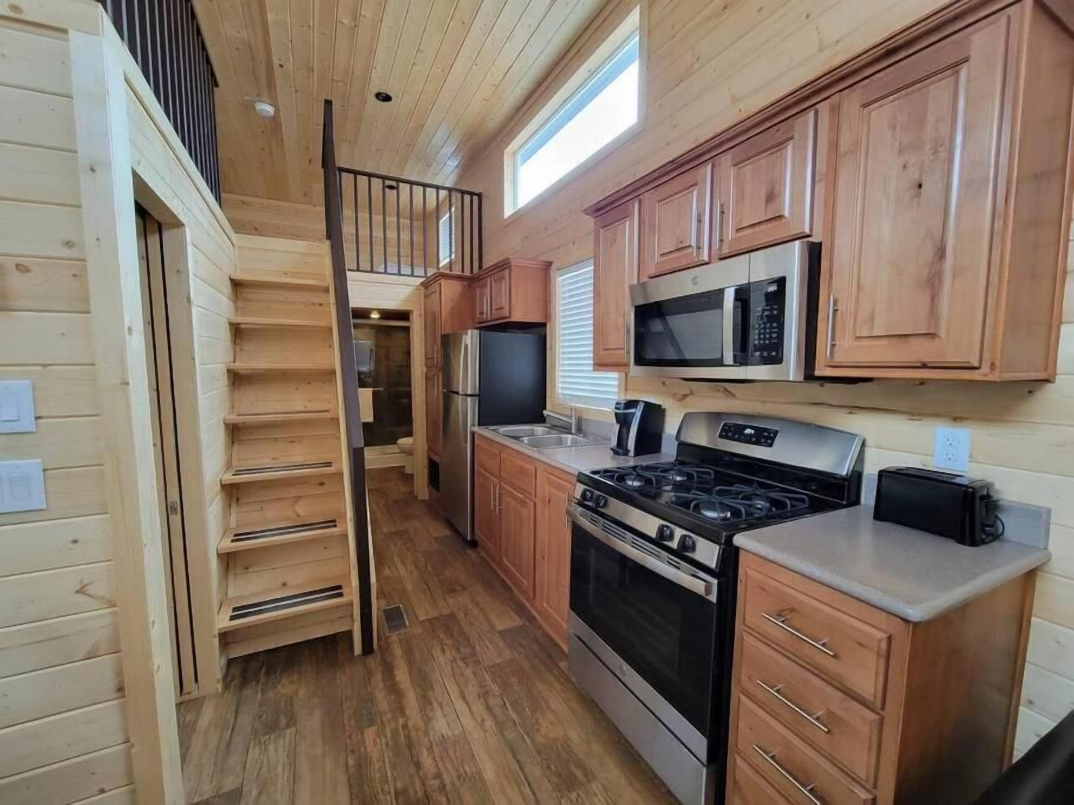 A compact kitchen with wooden cabinets, a microwave, a stove, and a refrigerator.