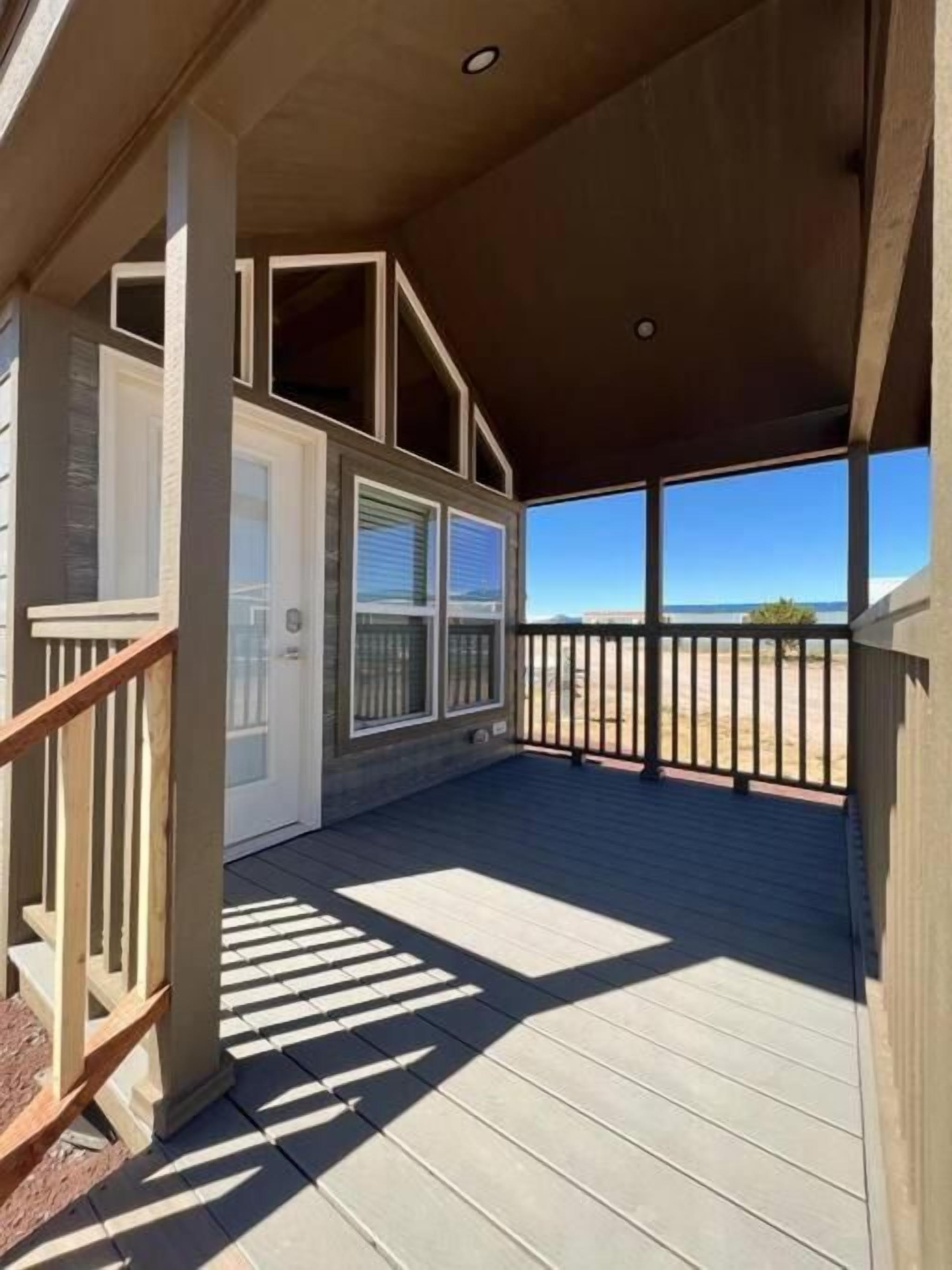 A covered deck with a view of the landscape, wooden railings, and a door leading to an interior space.