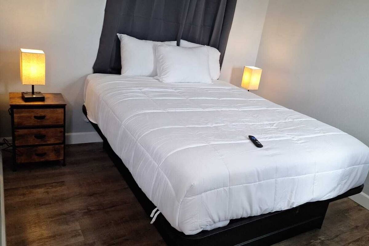 A neatly made bed with white bedding and a black headboard, flanked by two bedside tables with lamps.