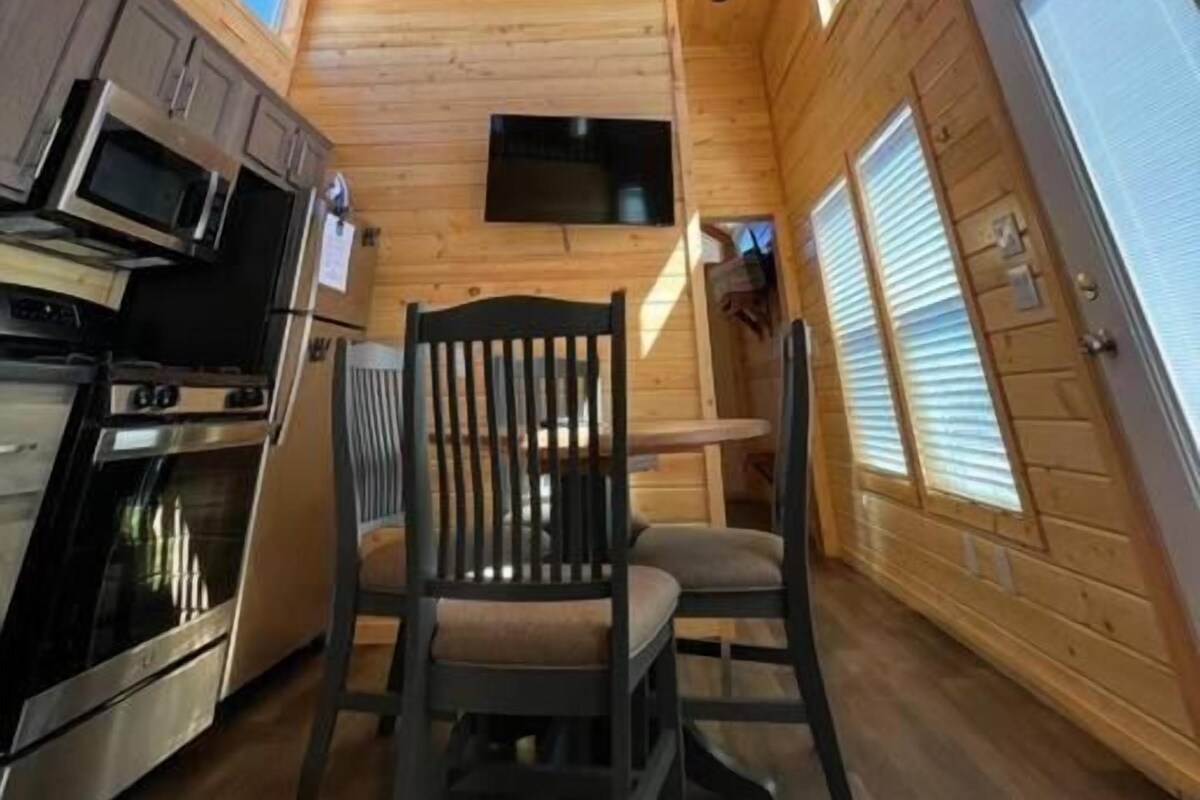 A cabin interior with a kitchen area, dining table, and a ceiling fan.