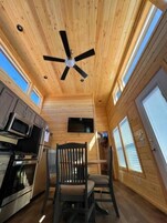 Interior de una cabaña con cocina, mesa de comedor y ventilador de techo.