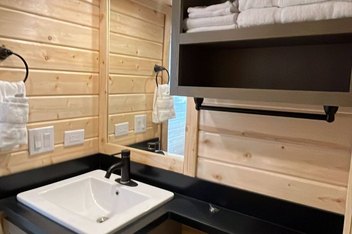 A wooden cabin bathroom with a sink, toilet, and a shelf with folded towels.