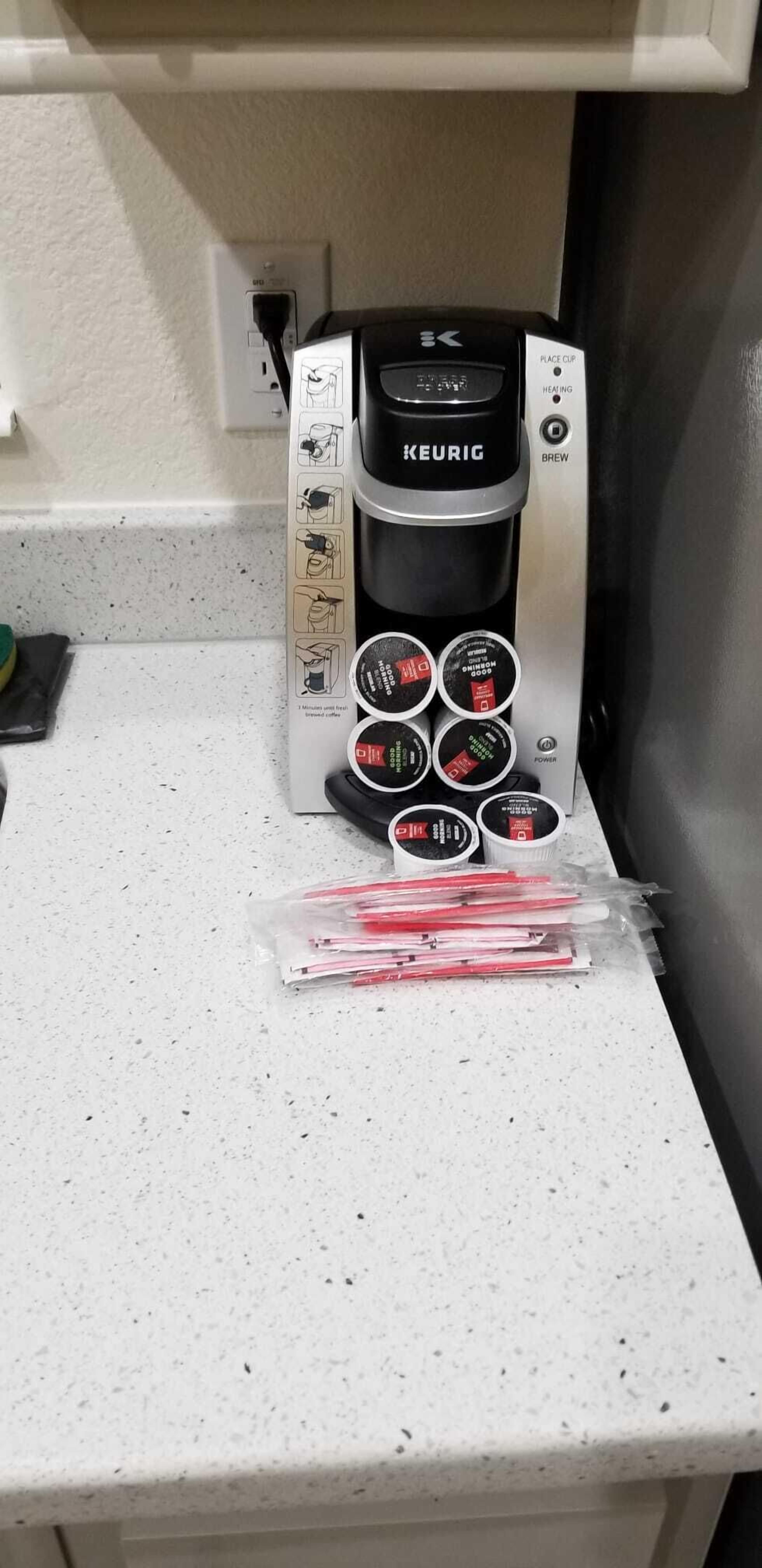 A Keurig coffee maker on a kitchen counter with a coffee pod holder and a bag of red straws.