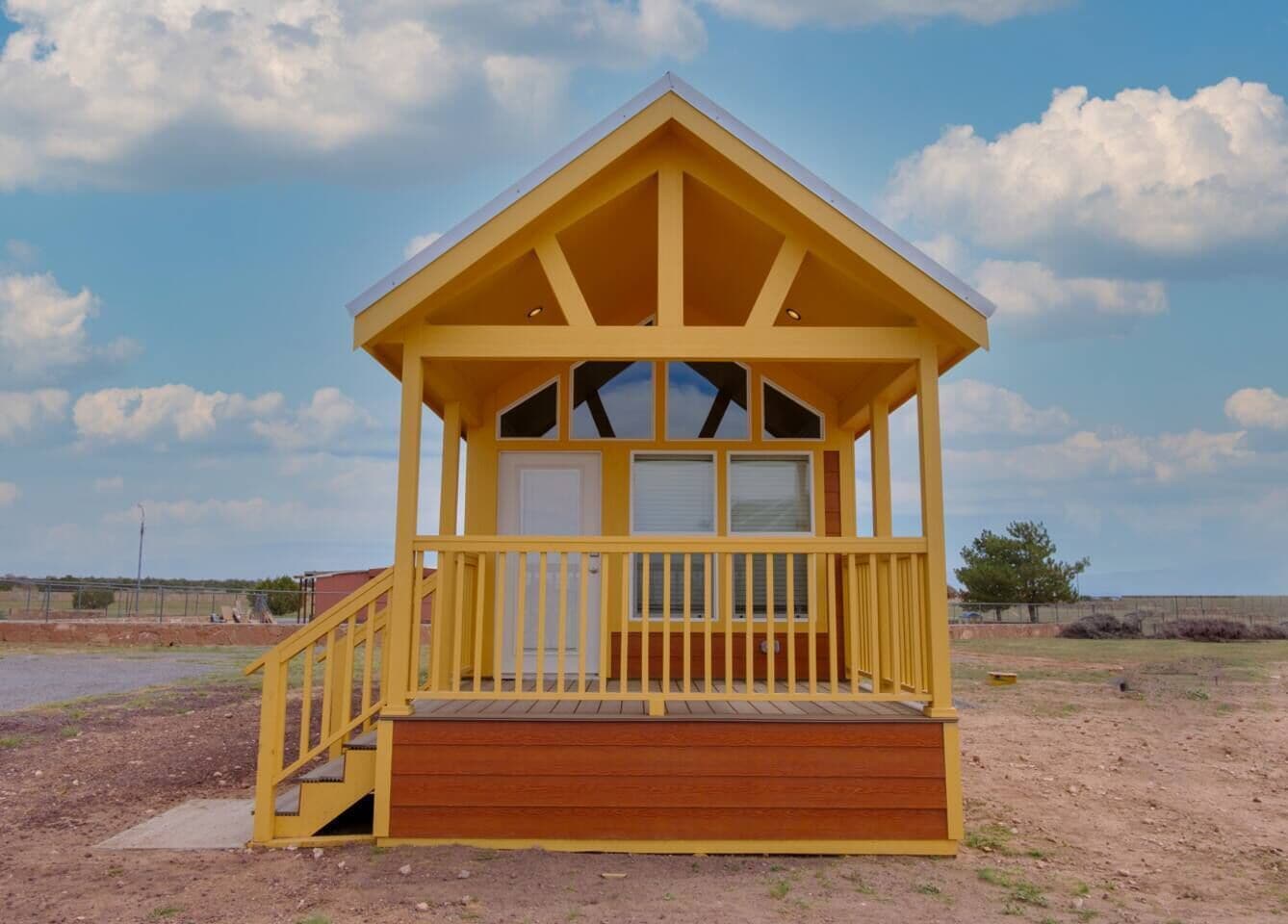A yellow wooden structure with a porch, a door, and windows.