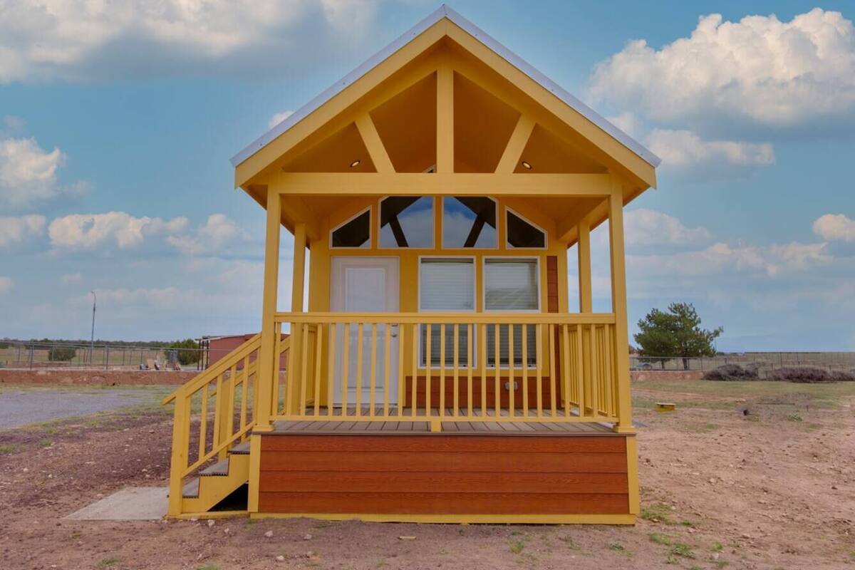 A yellow wooden structure with a porch and a door, set in a dry, open landscape.