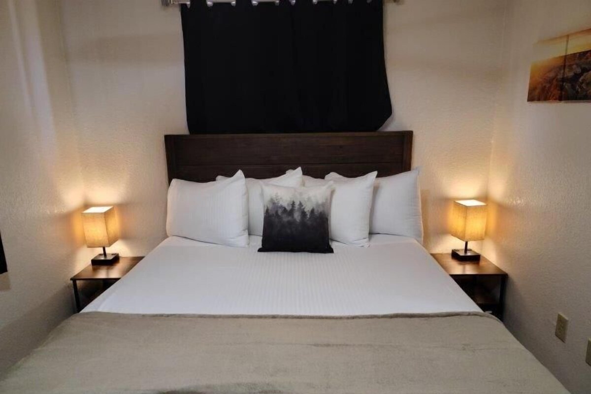 A hotel room with a large bed, two bedside tables with lamps, a dark headboard, and a painting on the wall.
